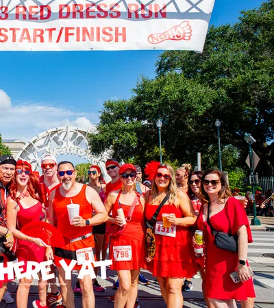 Group of people dressed in red at the NOH3 Red Dress Run start/finish line outdoors on a sunny day.