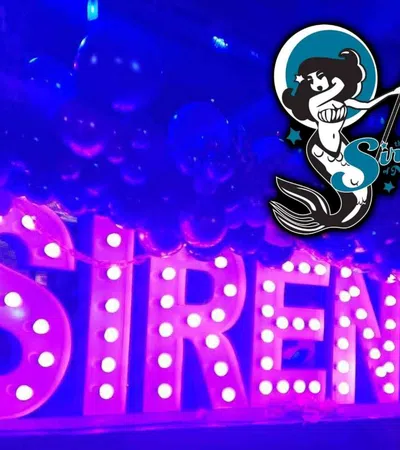 Illuminated marquee letters spelling SIRENS surrounded by balloons with The Sirens logo in neon blue and purple lighting.