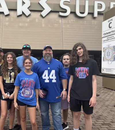 Group of New Orleans Saints and New York Giants fans posing outside Caesars Superdome stadium entrance.
