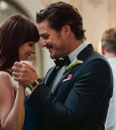 Couple in formal attire dancing closely and smiling at a romantic indoor event with other guests in background