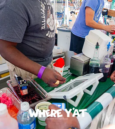 People preparing colorful snow cones at a festive outdoor event.