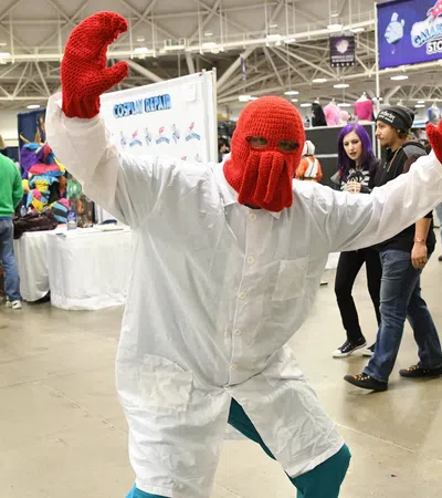 Person dressed as Dr. Zoidberg in a white lab coat and red knitted mask at a convention.