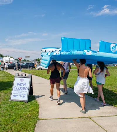 Group carrying large blue float at summer event with a closed path sign in the background.