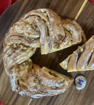 Glazed cinnamon roll wreath with nuts sliced on a wooden board over red cloth background