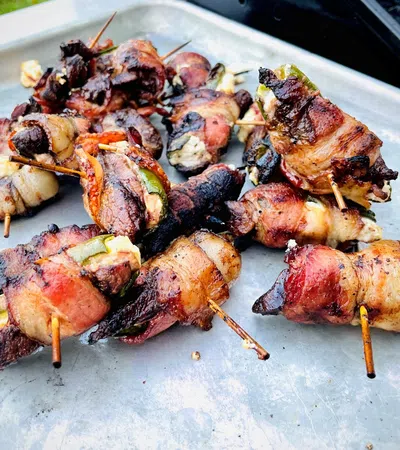Grilled bacon-wrapped jalapeño poppers on a metal tray with toothpicks, showing charred and crispy textures.