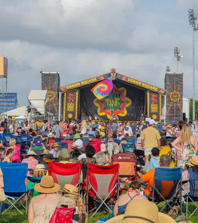 Crowd enjoying a music festival under sunny skies, featuring vibrant stage decorations and tents.