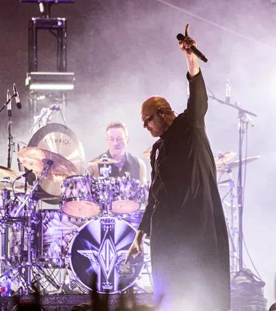 a person holding a microphone and standing next to a person playing drums