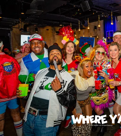 Group of people in colorful costumes enjoying a lively indoor party with themed decorations and drinks.