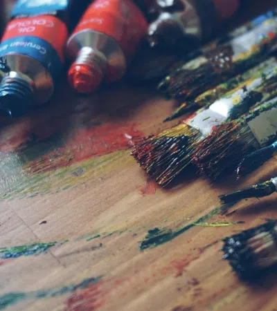Assorted paint tubes and brushes on a wooden surface, showcasing vibrant colors and textures.