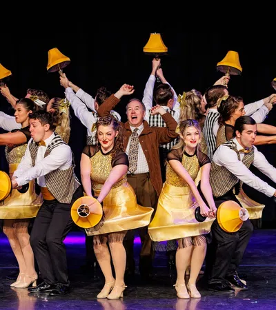 Performers in gold costumes dancing with yellow bell lamps on stage during a theatrical musical number