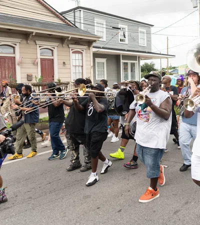 Street parade with musicians playing brass instruments and a cameraman filming the lively event.