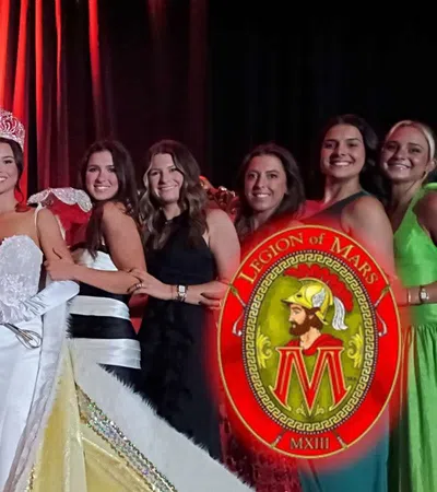 Group of people dressed formally with one man in Roman soldier costume and a crowned woman in white gown.