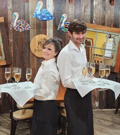 a man and woman standing next to each other at a table with wine glasses