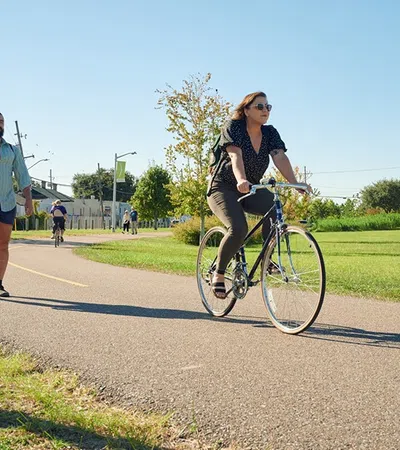 a woman riding a bicycle on a road with a man walking behind her