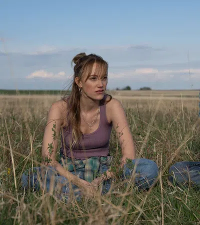 Young man and woman sitting in a grassy field talking under a partly cloudy sky on a sunny day