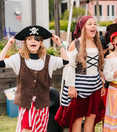 Group of children dressed as pirates and a mermaid performing outdoors with joyful expressions