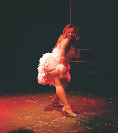 Woman in white feathered costume performing a dance on stage lit with red spotlight.