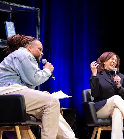 Two people on stage during a lively interview with books displayed on shelves and blue curtains in the background