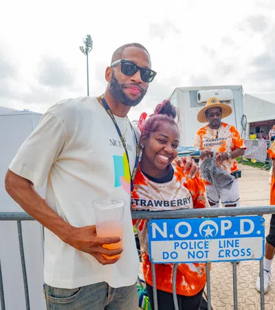 A smiling couple at a festival pose near a police barrier with festival staff in vibrant shirts in the background.