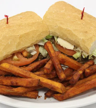 Sandwich with lettuce, tomato, and meat served with a side of crispy sweet potato fries on a white plate.