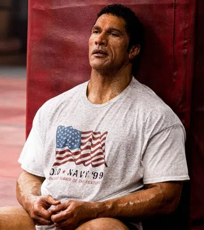 Man in a white USA flag T-shirt resting against gym equipment in a workout space