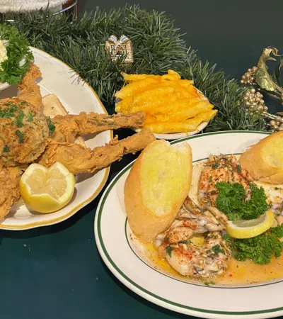 Plates of stuffed crab claws with toast, cocktail sauce, and macaroni and cheese on a green table with decorative greenery.
