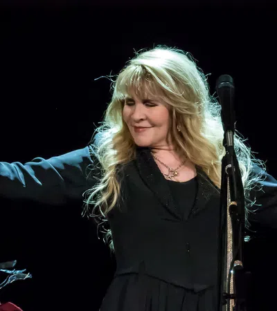 Female singer with long blonde hair performs on stage holding decorated microphone stand under spotlight.