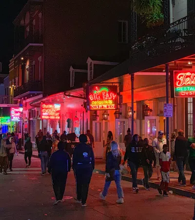 Busy night street scene with neon signs and people walking outside bars and restaurants in the French Quarter New Orleans