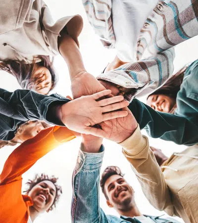 Group of diverse young people standing in a circle with hands joined together in unity and teamwork.