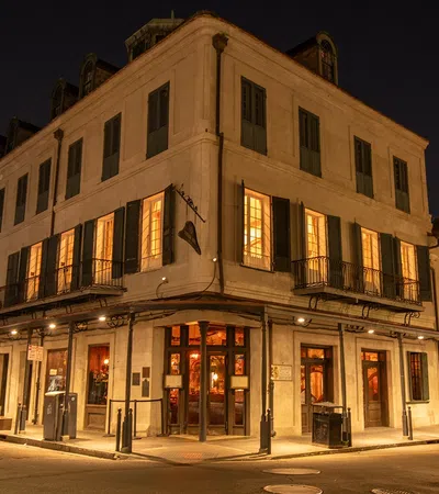 Historic corner building at night with warm lit windows and parked cars on street in a lively city area