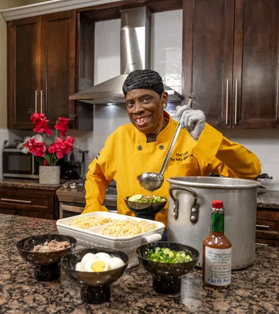 Chef in an orange shirt prepares dishes in a modern kitchen with fresh ingredients and vibrant decor.