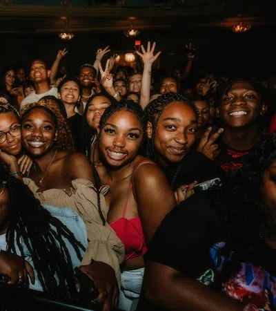 Group of diverse friends smiling and posing closely together at a lively indoor event with warm lighting.