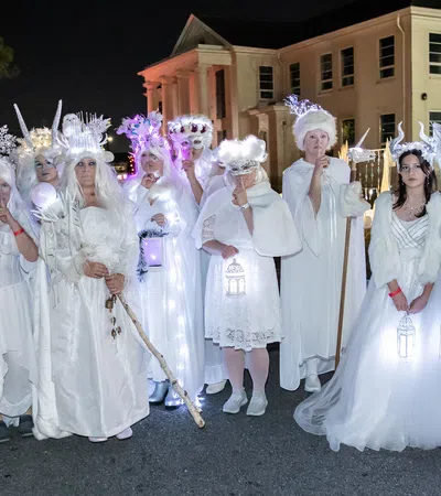 Group of people in elaborate white costumes and glowing accessories posing outdoors at night near a building