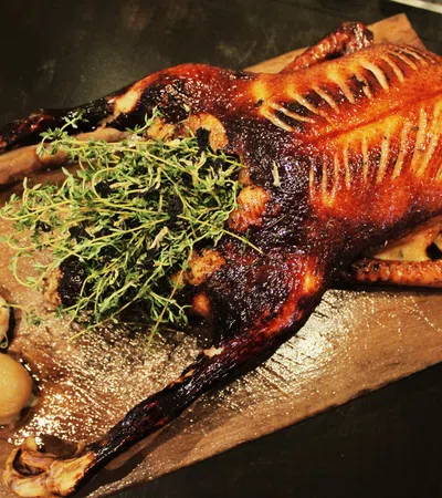 Whole roasted duck with crispy skin garnished with fresh herbs served on wooden board with garlic and onion.