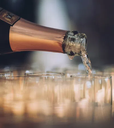 Champagne being poured from a bottle into a row of clear glasses at a celebration or event.