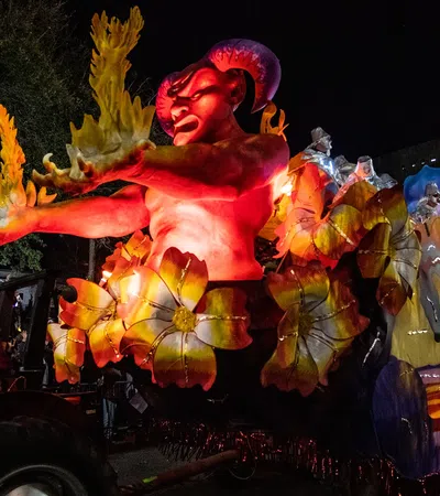 Illuminated red demon float with yellow flowers and flames at a night parade with spectators in background.