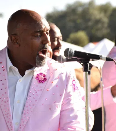 Male singers in matching pink embellished suits performing passionately at an outdoor event with microphones.