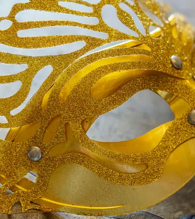 Close-up of an ornate golden masquerade ball mask with glitter and intricate cut-out patterns.