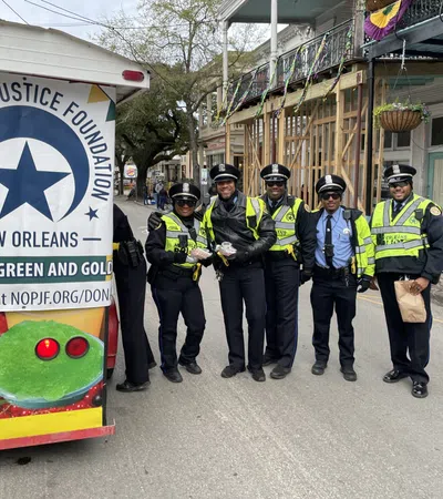 Five New Orleans police officers standing on a street beside a Police and Justice Foundation sign and Mardi Gras decorations.