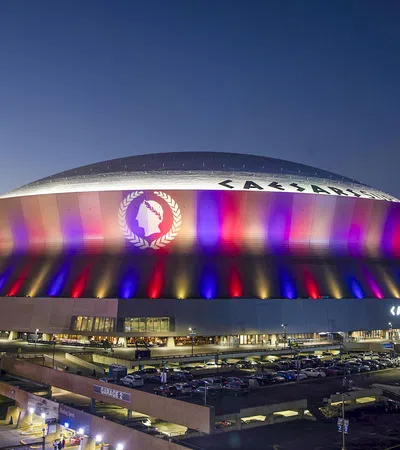 Caesars Superdome lit up with red, blue, and yellow lights at dusk in New Orleans, Louisiana.