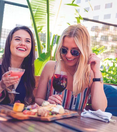 Three young women enjoy drinks and appetizers at an outdoor restaurant on a sunny day