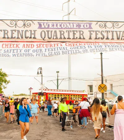 Crowd entering French Quarter Festival under welcome banner with security check and streetcar in background