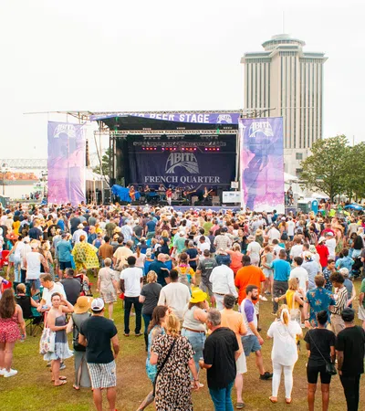 Large crowd enjoying live music at an outdoor festival near a waterfront stage and city skyline.