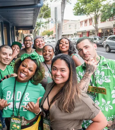 Group of diverse people dressed in green celebrating and smiling outdoors on a city street party.