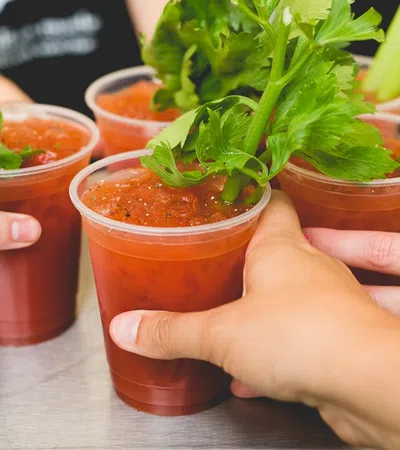 Group of hands toasting with refreshing Bloody Mary cocktails garnished with celery.
