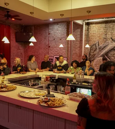 People socializing and enjoying drinks around a modern bar with exposed brick walls and warm pendant lighting.