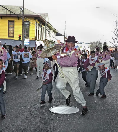 Children and adult dancers in traditional costumes perform on a street during a lively parade with onlookers.