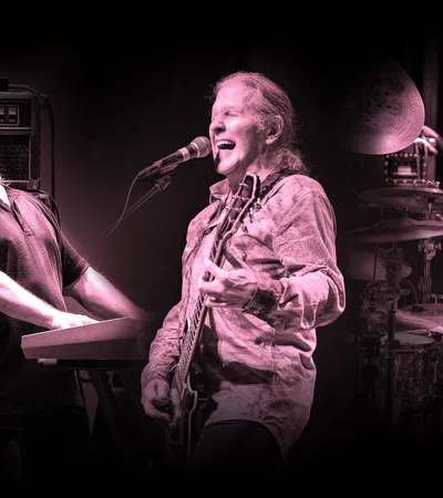 Three musicians passionately playing keyboard, guitar, and drums during a live performance with black background.
