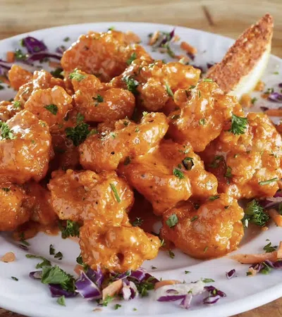 Buffalo cauliflower bites garnished with parsley and shredded vegetables on a white plate with a breadstick.