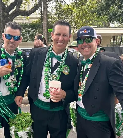 Group of men in formal wear with green accessories celebrating outdoors during a festive parade or event.